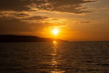 A young man's silhouette, deep in thought, against the backdrop of a dramatic tropical sunset over the calm ocean, capturing a tranquil moment of peaceful reflection