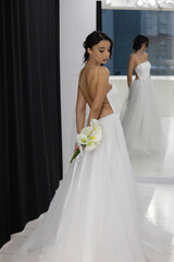 Stylish bride in open back wedding dress with bouquet posing gracefully indoors