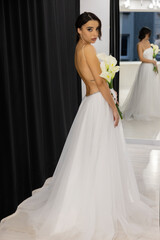 Chic fashion model posing in elegant open back wedding dress with flowers