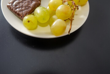 White grapes and chocolate biscuits on the same plate as two contrasts of healthy and unhealthy sugars and so-called treat foods on a dark background