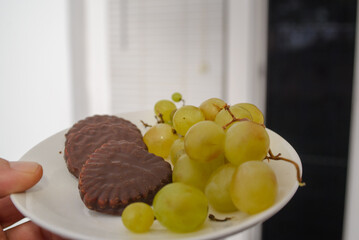 White grapes and chocolate biscuits on the same plate as two contrasts of healthy and unhealthy sugars and so-called treat foods on a dark background