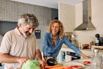 Portrait of happy senior mid aged mature couple prepering meal with fresh vegatebles in kitchen at hpme