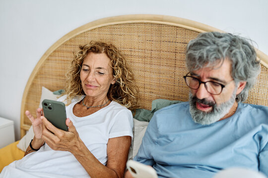 Senior middle aged couple using phone in bed in bedroom