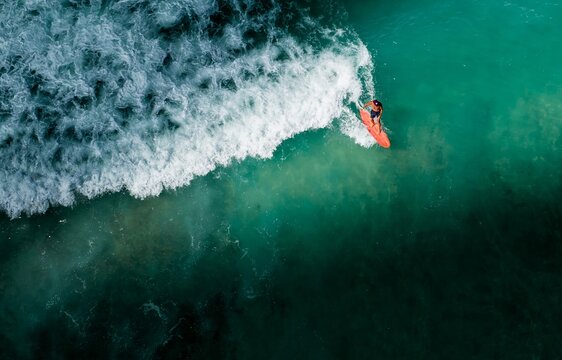 Aerial view of a lone surfer riding a turquoise wave, the white foam contrasting against the deep ocean, creating a dynamic scene, Waikiki, Honolulu, Hawaii, United States.