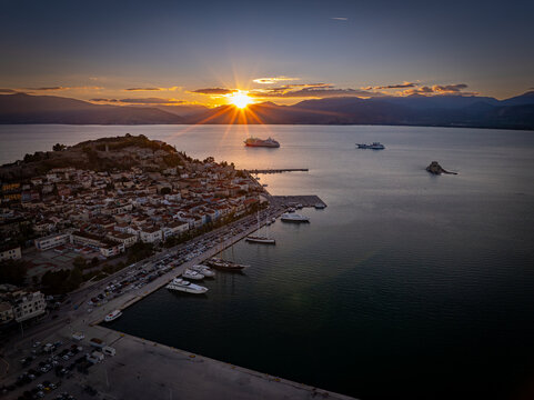 Aerial view of the sun setting behind Bourtzi castle and the old town of Nafplio, painting the sea with fiery hues, Argolis, Greece.