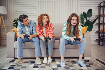 Obraz premium Funny young people engaged in a video game competition, sitting on a cozy couch in a modern living room.