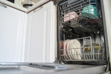 Open dishwasher with clean dishes and cups in modern kitchen setting.