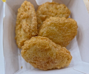 Golden-brown, deep-fried chicken nuggets  inside a white, disposable cardboard container. 