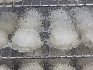 Close-up, horizontal view of steamed white buns ( baozi) resting on wire racks inside a steamer or...