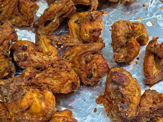A close-up, overhead view of a collection of deep-fried chicken pieces, primarily wings and portions, scattered across a reflective aluminum foil-lined tray.