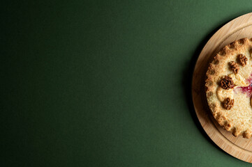 Top view of a rustic homemade pie with walnuts on dark green background with copy space.