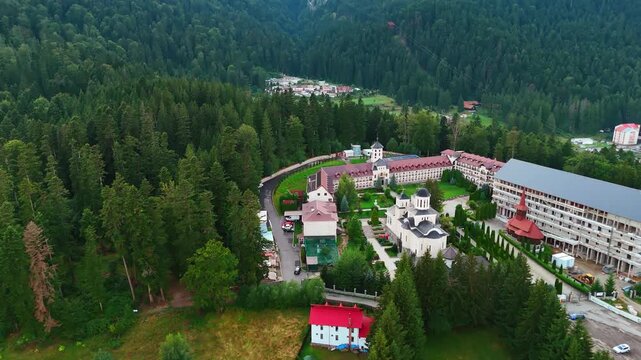 Beautiful buildings and churches on the mountain surrounded by the pine tree woods. Drone flight above Busteni, Romania.