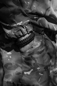 A powerful close-up in black and white shows a soldier's hand and a paracord survival bracelet against a tactical camouflage uniform.

