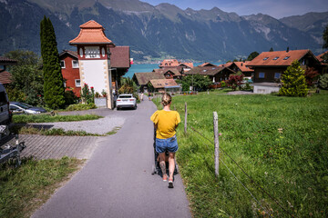 Mujer caminando con hija en carriola en Pueblo suizo con montañas lago banderas y bote en el agua....