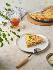 Sliced ​​shortcrust pastry tart with rhubarb, plum jam, and almonds on a plate against a light concrete background.