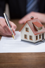 Fototapeta premium Home contract signing: Pen hovers above paperwork next to a miniature house, symbolizing a major life decision.