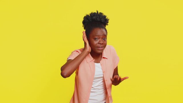 What. I cant hear you. African woman leans forward with hand cupped to ear, expressing confusion curiosity. Black girl on yellow background shows surprise effort to understand unclear sound or speech