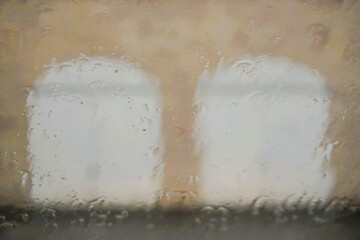 Abstraktes Motiv mit Wassermuster auf Glasscheibe vor beige-brauner Scheunenwand mit zwei weißen Holztoren bei Regen und Sturm am Nachmittag im Herbst