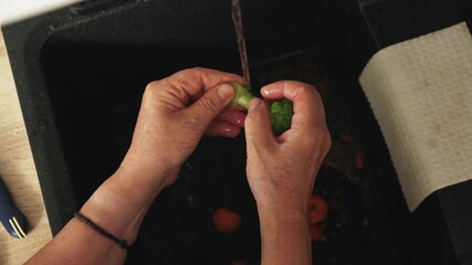 Hands are shown rinsing fresh vegetables under running water in a kitchen sink. - Powered by Adobe