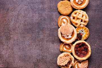 Thanksgiving or autumn dessert side border. Overhead view against a dark background. Pumpkin, apple and pecan mini pies, turkey, leaf and snickerdoodle cookies, pumpkin rolls.