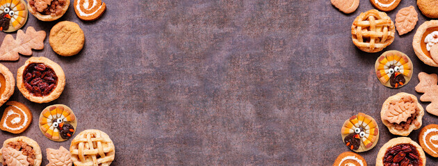 Thanksgiving or autumn dessert double border. Top down view against a dark banner background. Pumpkin, apple and pecan mini pies, turkey, leaf and snickerdoodle cookies, pumpkin rolls.