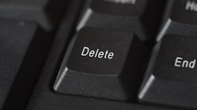 Finger presses delete key on black keyboard symbolizing digital termination and control in computer technology input and data management tasks