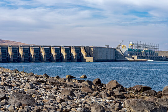 The rocky shoreline of the Columbia River faces the Wanapum dam spillway and powerhouse in Washington, USA