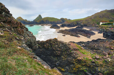 Kynance Cove, seen from a rocky hill near. Green blue sea water washes smooth sand with some large rocks over near