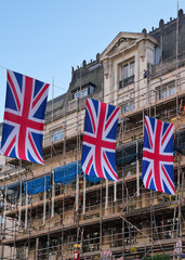 British Union Jack flags hanging above main street in London after king coronation, scaffolding on a building at background