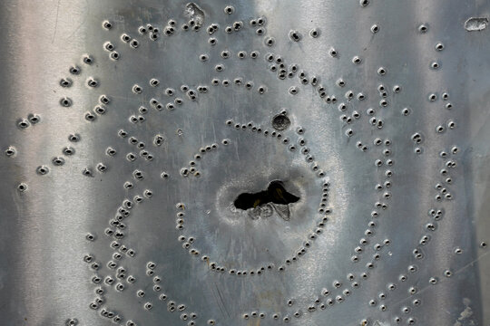 Thick steel plate with holes from firing different ammo types after ballistic penetration test