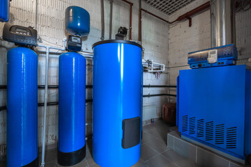 A mechanical room showcases a hot water system with blue tanks and a boiler. The setup highlights efficient equipment and organized piping in a clean, functional space