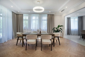 This bright dining room features a stylish table surrounded by chairs, ample natural light from large windows, and modern decor that creates a welcoming atmosphere for meals