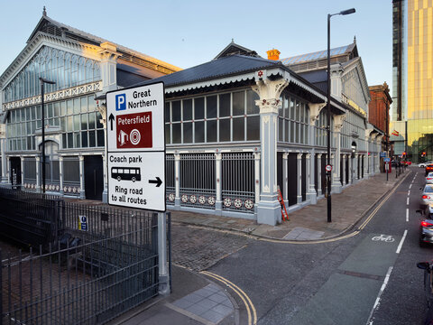 Historic glass Upper Campfield Market Hall  building in Manchester with street signs, pedestrians, and coach park