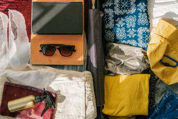 Yellow suitcase inside a seaside apartment room with minimalist interior, balcony, bright vacation items, white sheer curtains, and sunlight casting beautiful shadows
