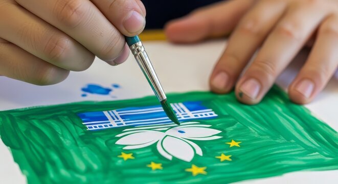 Closeup of a childs hand painting the flag of macau with a paintbrush on a white paper surface