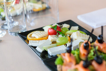 gourmet cheese platter with brie, blue cheese, and cheddar served with grapes and cherry tomatoes on a modern black plate for a wine tasting event