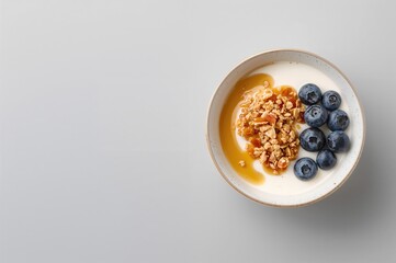 Morning yogurt bowl topped with granola, blueberries, and maple syrup on a gray surface, overhead shot with space for text. Nutritious eating theme.