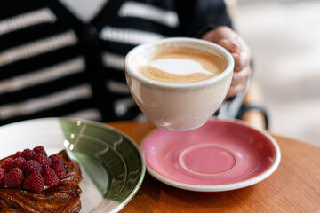 Woman drinking latte with raspberry pastry for breakfast