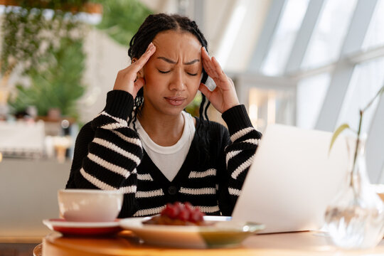 Woman suffering headache working on laptop in cafe