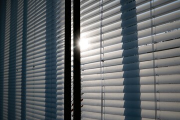 Contemporary room design featuring white blinds and black metal window frames, with sunlight creating captivating shadows through the Venetian shutters