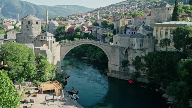 Mostar, Bosnia and Herzegovina Aerial drone video zooming out from the Old Bridge with the Neretva River below, revealing Koski Mehmed Pasha Mosque and the hills of Vihovići and Via Ferrata.