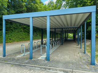 Covered bike rack structure in a serene outdoor setting surrounded by lush greenery on a sunny day