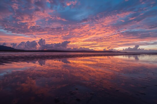 Stunning sunset with vivid orange, pink, blue, and purple clouds mirrored in sandy rain puddles - Powered by Adobe