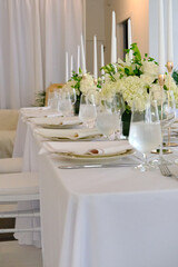 Elegant indoor wedding table setup featuring white roses and hydrangeas, gold candle holders with taper candles