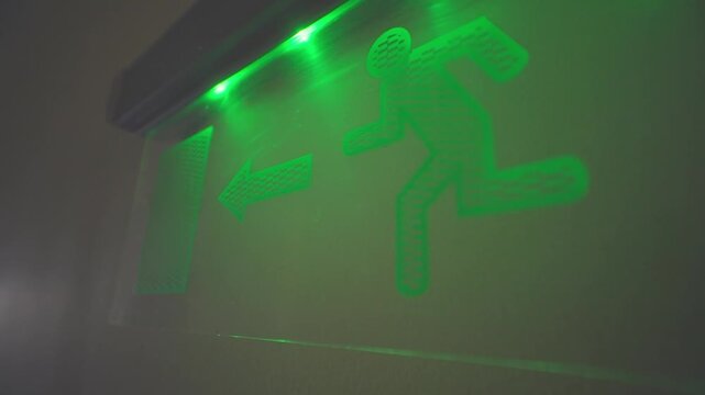 Green illuminated fire escape sign hang on the wall in the office building