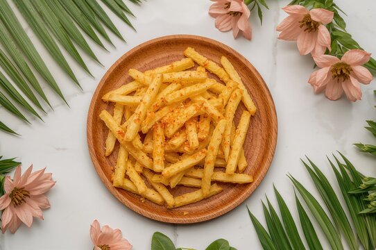 Crispy small French fries seasoned with spicy balado served on a wooden platter with artificial floral accents against a clean white backdrop