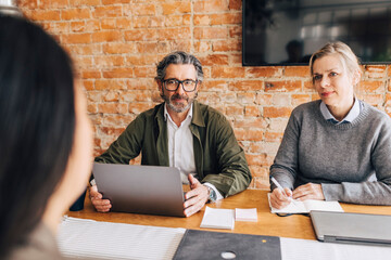 Senior businesswoman writing notes while sitting near male colleague and taking interview of new female hire in office