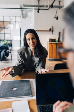 Woman gesturing while answering questions during interview with business experts while sitting at table in office