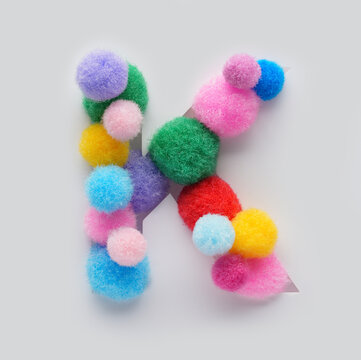 Colorful letter K made of fluffy pom poms on white background. Creative handmade typography for kids learning alphabet, educational design, playful classroom decor, and graphic projects.