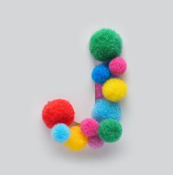 Colorful letter J made of fluffy pom poms on white background. Creative handmade typography for kids learning alphabet, educational design, playful classroom decor, and graphic projects.